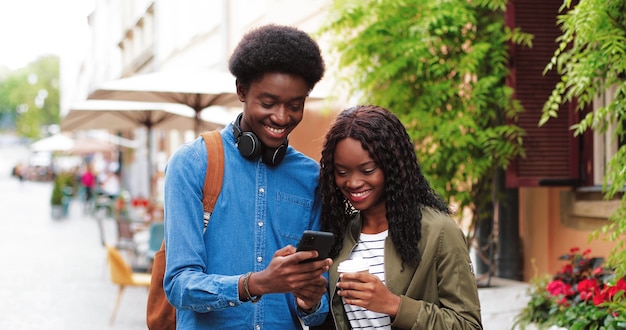 Stylish multiracial man and his girlfriend using his smartphone while walking down the street handso...