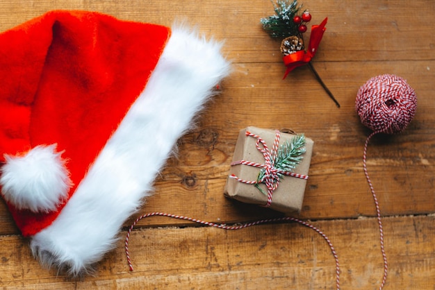 Stylish packaged Christmas gift box, Santa Claus hat and a sprig of spruce on a rustic wooden table. Atmospheric image. Merry Christmas and Happy Holidays, Happy New Year