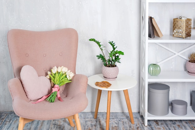 Stylish pink armchair with heart shaped pillow in a bright minimalist interior.