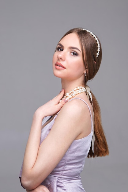 Stylish portrait of a beautiful girl with clean skin Studio portrait of a young girl with a diadem and pearl necklace on a gray background place for advertising