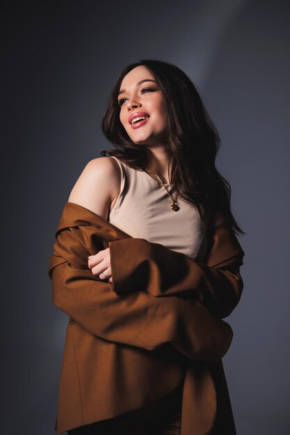 Stylish pretty young woman in brown classic suit sitting on gray background Beautiful woman in a jacket and with makeup on her face