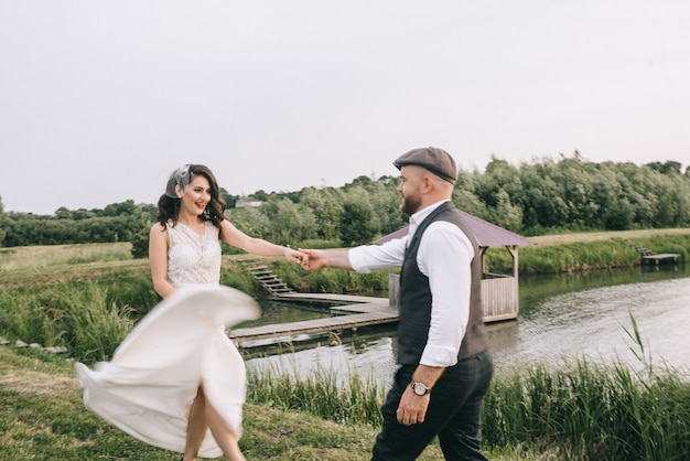 Stylish retro wedding couple walking in a field near the lake