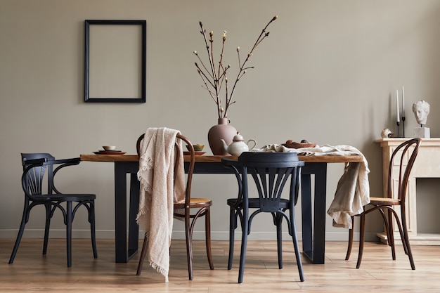 Stylish rustic interior of dining room with walnut wooden table, retro chairs, decoration, fireplace, dried flower, candlestick picture frame and carpet in minimalist home decor.