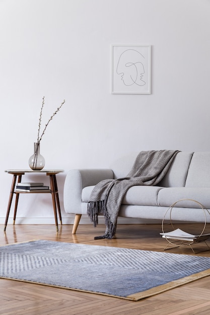 Stylish scandi interior of home space with design grey sofa, retro wooden table, mock up poster frame, decoration , carpet and personal accessories in elegant home decor.