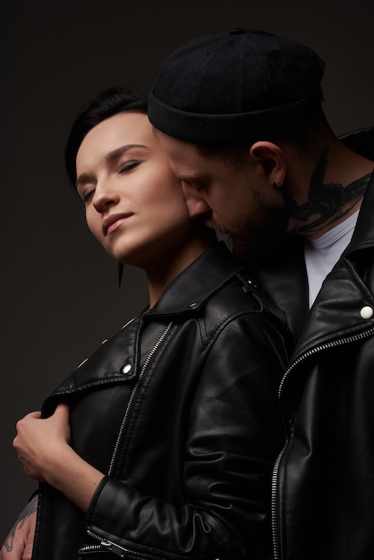 stylish and sexy punk couple on a dark studio background in leather jackets in tattoos the girl has red glasses