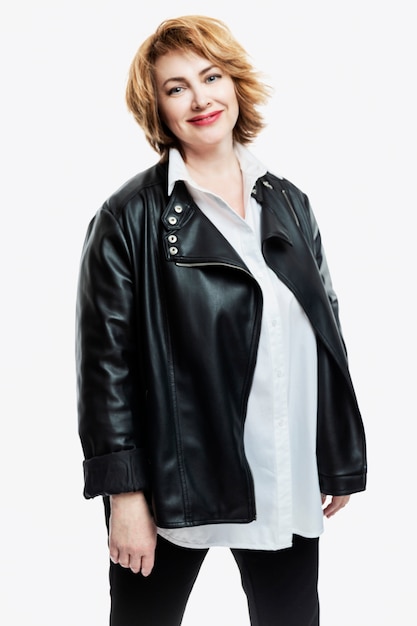 Stylish smiling middle-aged woman in a white shirt and a leather jacket on a white wall. Healthy lifestyle and activity. Vertical.