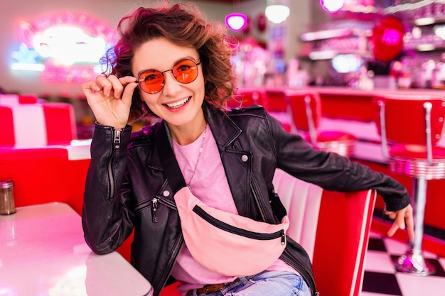 Stylish smiling woman in colorful retro vintage american 50's cafe sitting at table