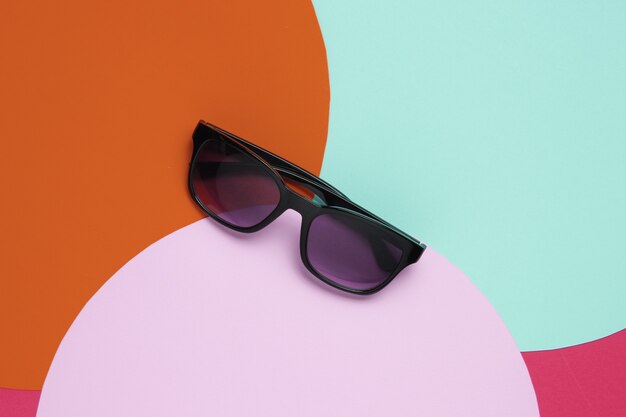 Stylish sunglasses on background with colored paper circles.  Flat lay fashion still life. Top view