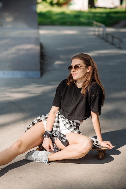 Stylish teenager girl with skateboard sitting and chilling in the skaters park