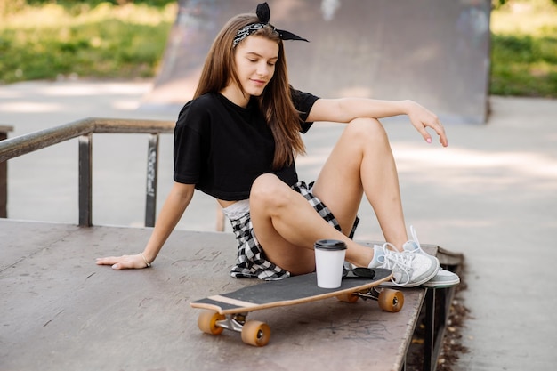 Stylish teenager girl with skateboard sitting and chilling in the skaters park