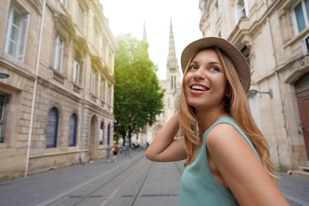 Stylish traveler girl turns around when walking in Bordeaux street with the cathedral on the background France