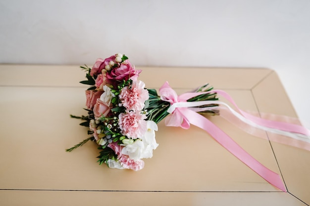 Stylish wedding bouquet bride of pink roses white carnation and green flowers and greens with ribbons lying on pastel table Close up Side view Wedding decor Artwork