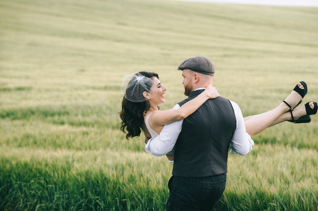 Stylish wedding couple in a  green field near retro car