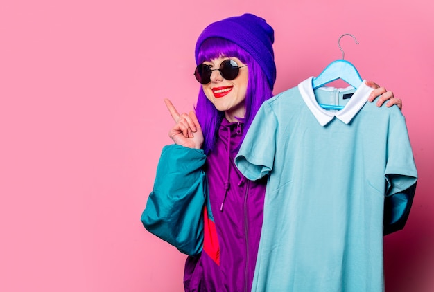 Stylish white girl in  tracksuit hold hanger with dress on pink wall