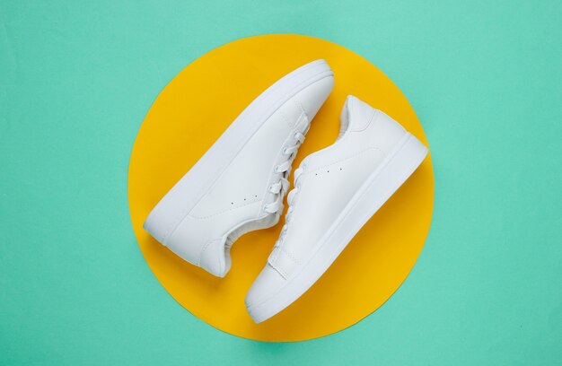 Stylish white sneakers on blue paper with yellow circle