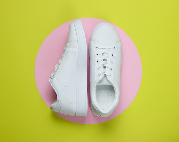 Stylish white sneakers on green paper with pink pastel circle