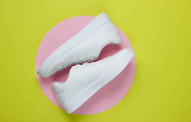 Stylish white sneakers on green paper with pink pastel circle