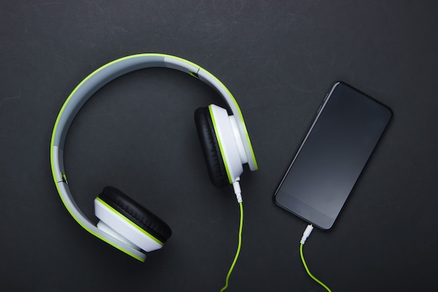 Stylish wired stereo headphones with smartphone on black surface