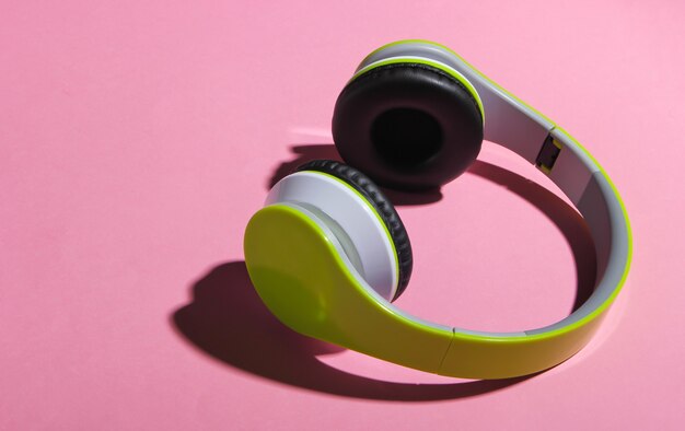 Stylish wireless stereo headphones with shadow on pink pastel surface