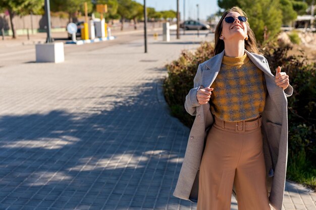 Stylish woman adjusting coat on street in sunny weather