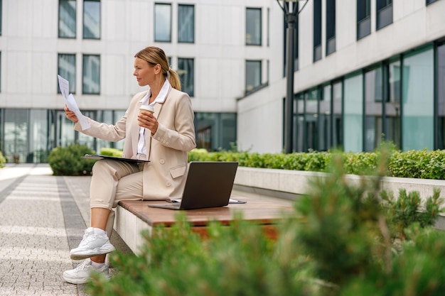 Photo stylish woman analyst working with documents while sitting outside on modern building background