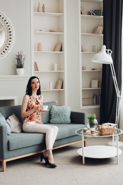 Stylish woman biting marshmallow on couch. casual clothing and heels sitting on modern couch with cushions and biting delicious marshmallow.