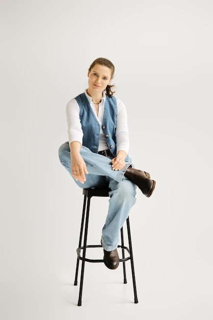 Stylish woman in denim vest and wide jeans sitting on a high chair