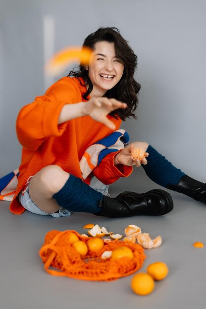 Stylish woman dressed in orange knitted jacket posing for a photo in a photo studio on a gray paper background Bright emotions poses modern concept