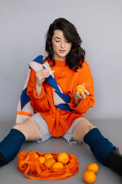 Stylish woman dressed in an orange knitted jacket posing for a photo in a photo studio