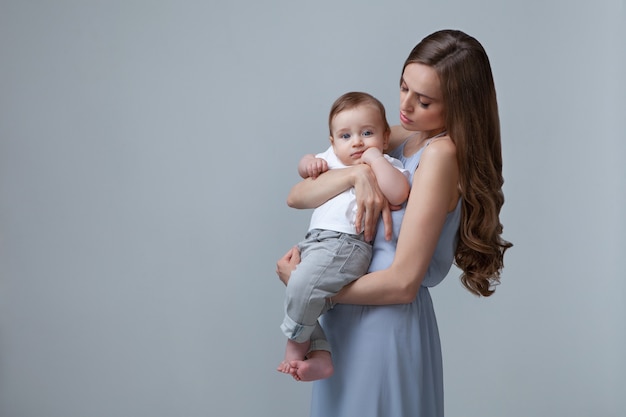 Stylish Woman holding small Baby isolated blue background Beautiful Mother and Son Caucasian Model