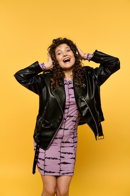 Stylish woman posing in leather jacket against a yellow wall