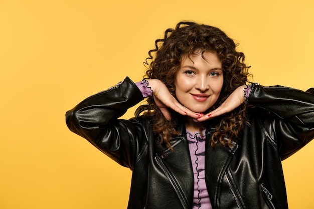 A stylish woman posing in a leather jacket against a yellow wall