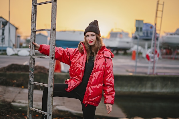 Stylish woman in red down jacket, hat on city street