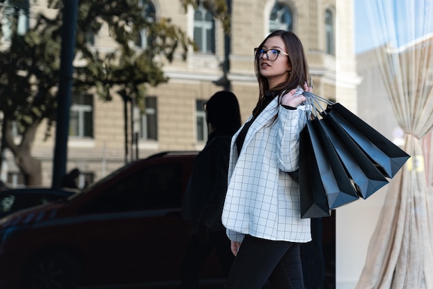 Stylish woman shopper with black bags. Beautiful girl near a fashion store. Black friday concept.