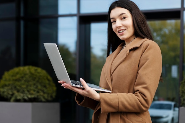 Stylish woman standing outdoors using laptop Businesswoman working on street online shopping