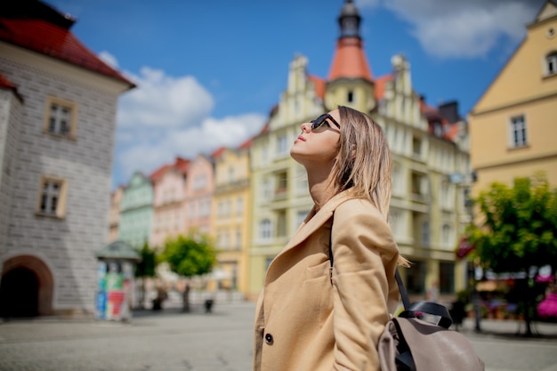 Stylish woman in sunglasses and backpack in aged city center square