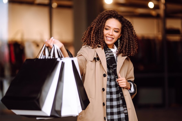 Stylish woman in trendy clothes with shopping bags near mall Woman after shopping