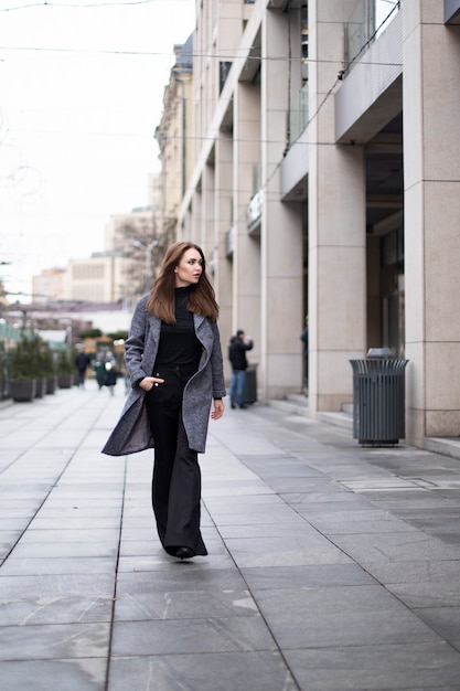 Stylish woman walks through the city in a coat. Free space for text