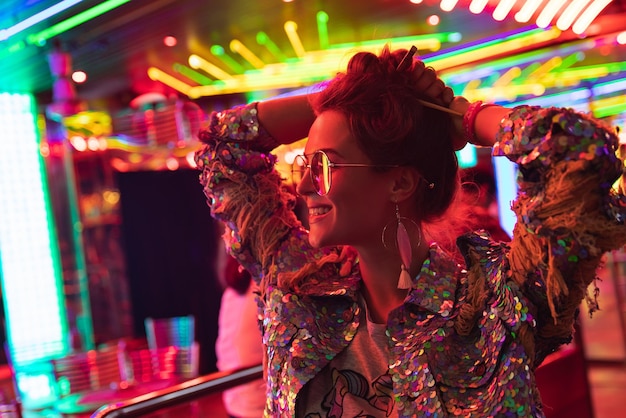 Stylish woman wearing jacket with shining sequins on the city street with neon lights