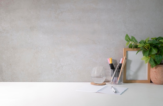 Stylish workplace with houseplant notebook and glass of water on white table Copy space for your text