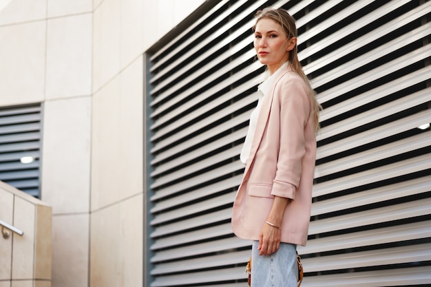 Stylish young businesswoman walking on the city street on sunny day