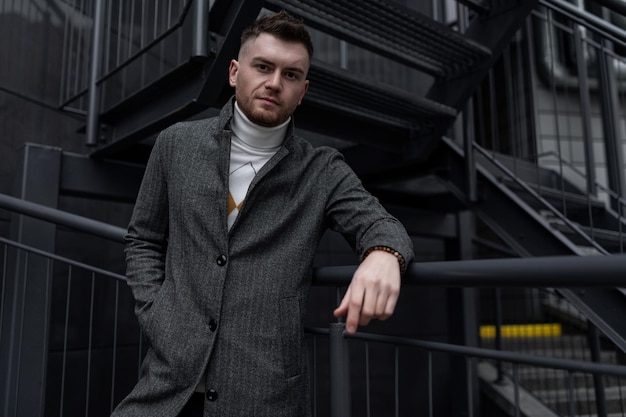 Stylish young caucasian he man in autumn coat on black stairs outside