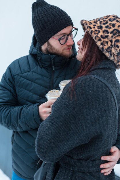 Stylish young couple of lovers in fashion winter clothes with a jacket are holding a cup of coffee and hugging on a white background