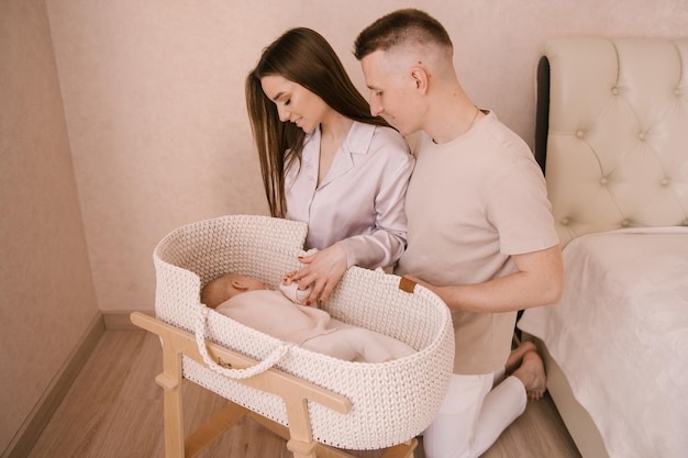 Stylish young family photographed with a little beautiful baby Family and parenting concept Parents put the baby to sleep in a baby cradle