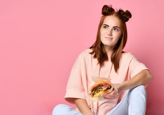 Stylish and young ginger Woman hold burger sandwich on pink background