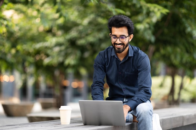 Stylish young indian man using laptop on the street