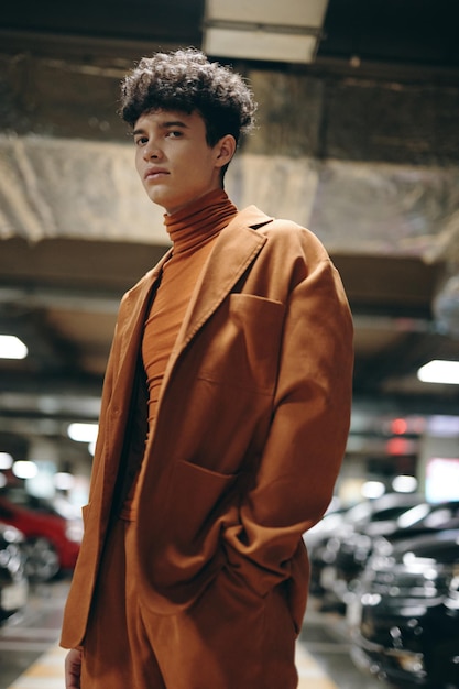 Stylish young man in a brown suit posing in an underground parking garage