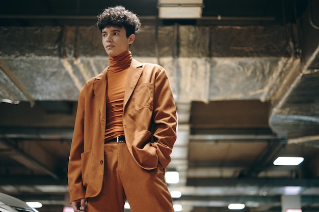 Stylish young man in a brown suit standing confidently in an urban parking garage