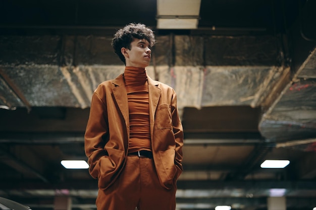 Photo stylish young man in a brown suit and turtleneck standing confidently in a modern underground