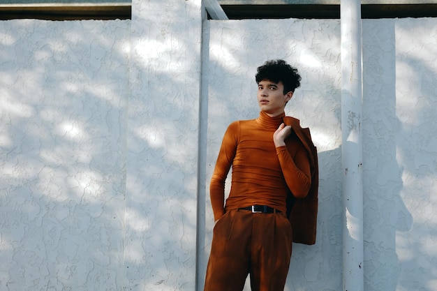 Photo stylish young man in brown turtleneck against a textured white wall